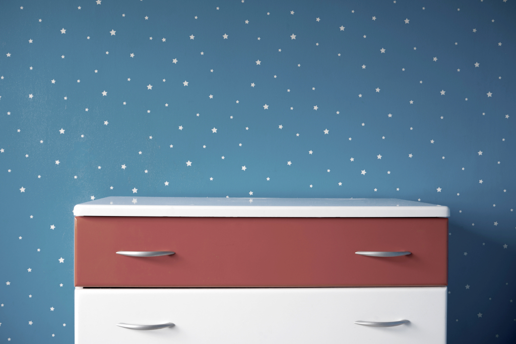 Mur avec papier peint étoilé et commode peinte.